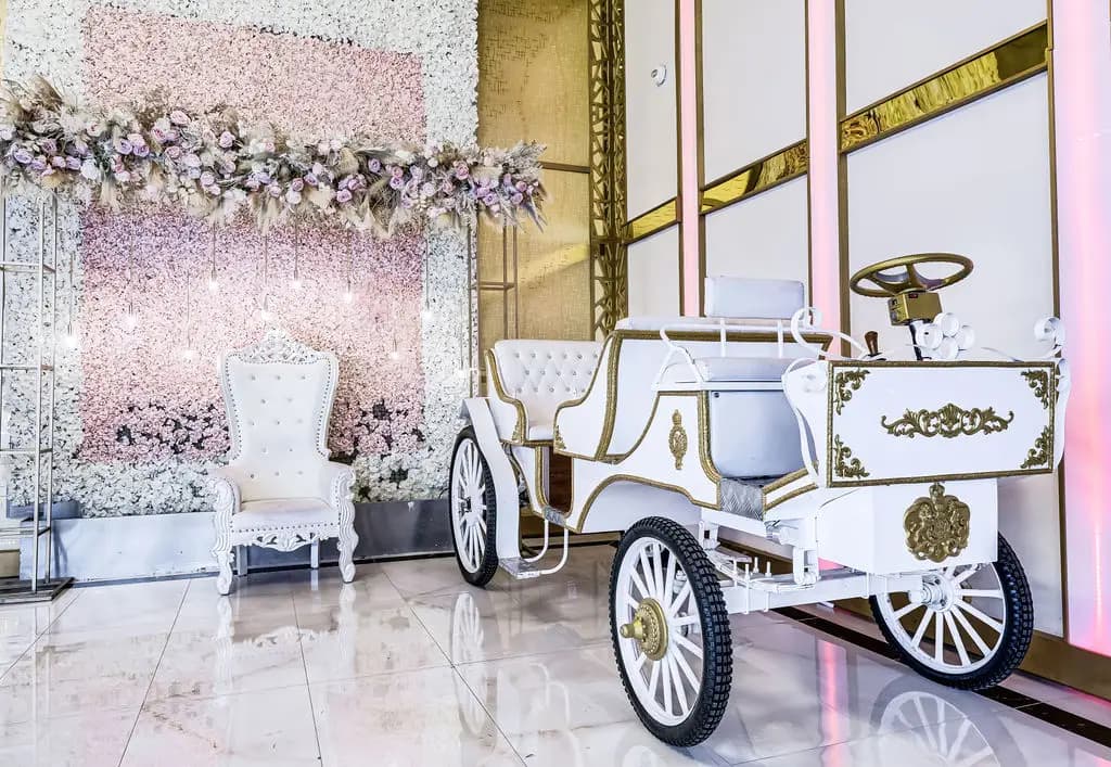 White ceremonial carriage and throne chair in front of a blush flower wall