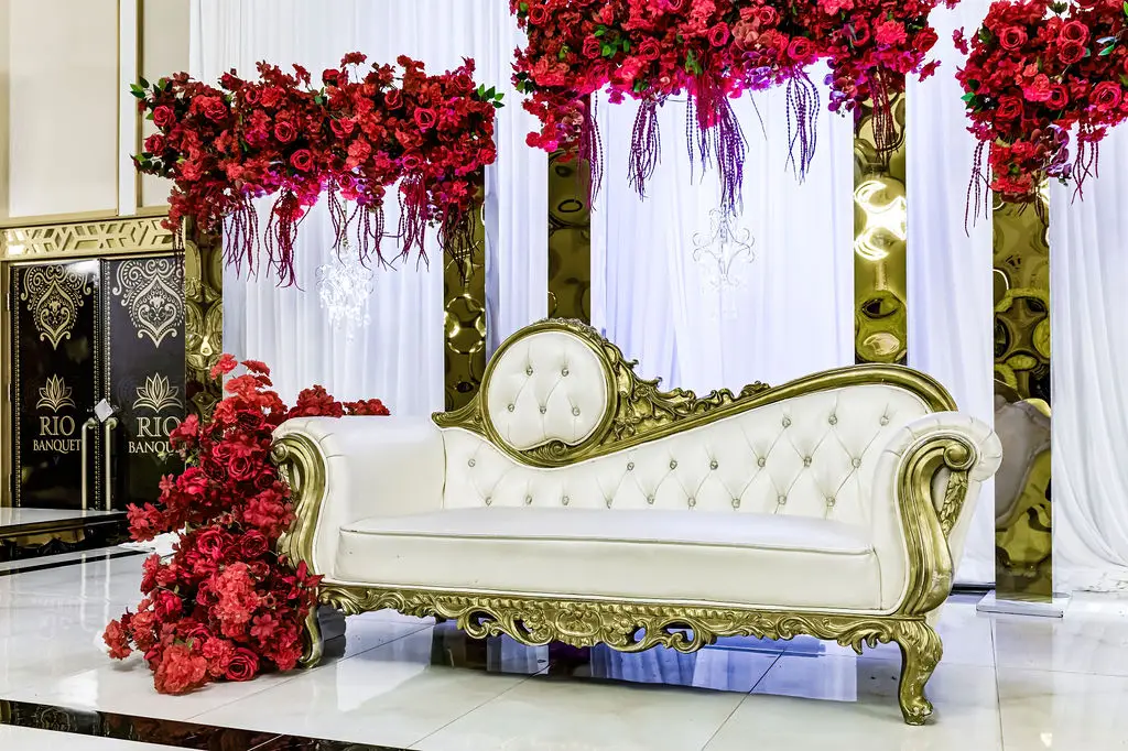 Reception stage with cascading red roses and an ivory tufted sofa