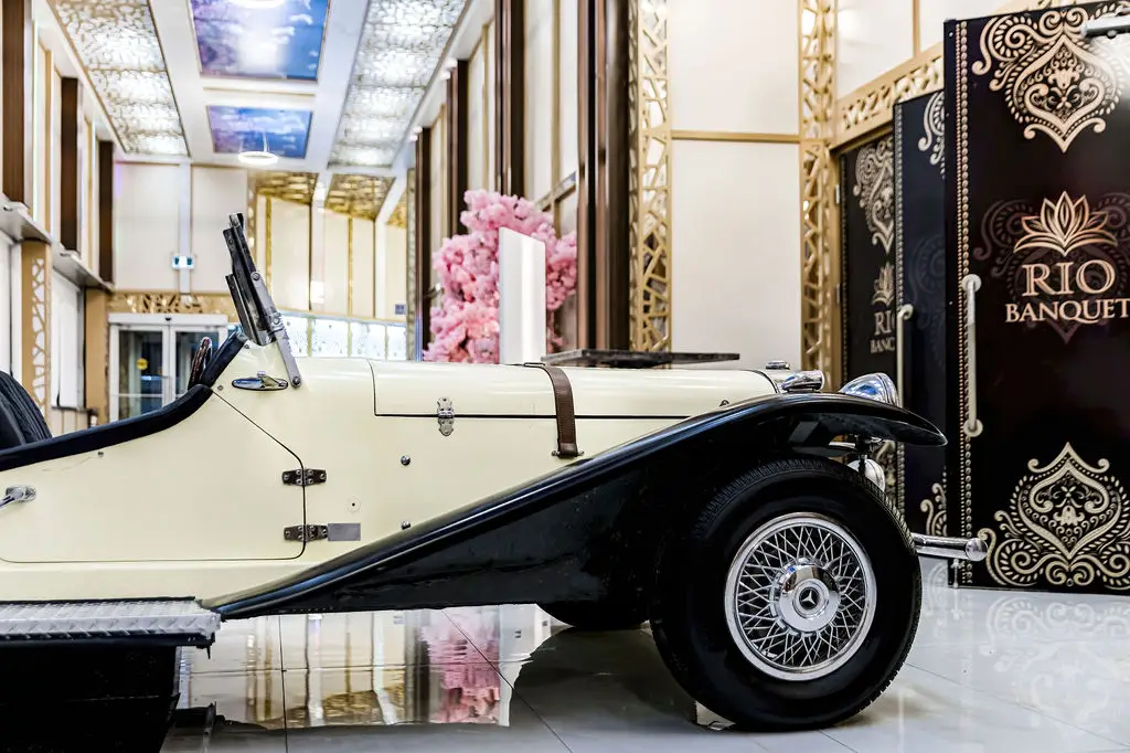Cream vintage car displayed in the marble lobby beside pink blossom décor