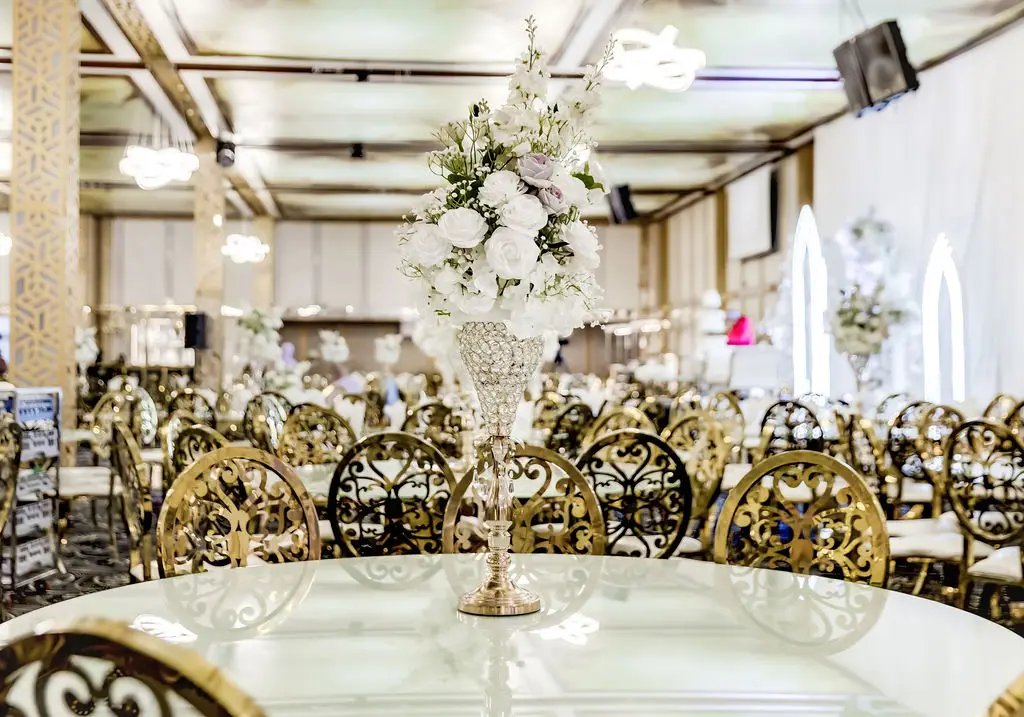 Banquet hall set with gold filigree chairs and a tall white floral centrepiece on a marble table